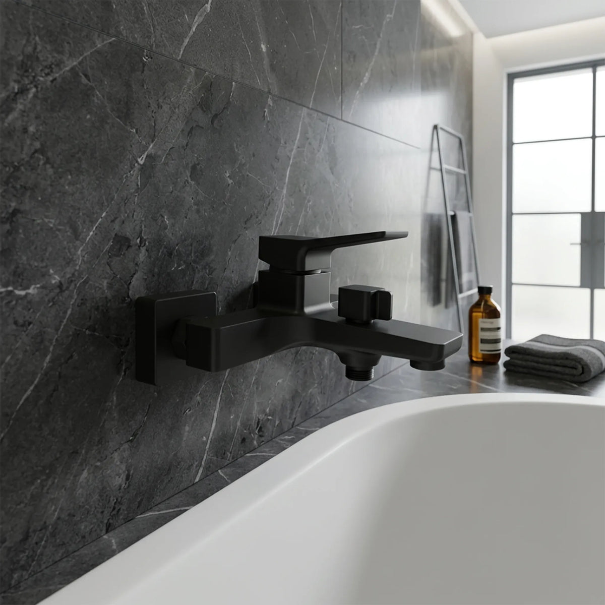 A matte black wall-mounted bathtub faucet installed above a white bathtub, set against a dark gray marble tiled bathroom wall.