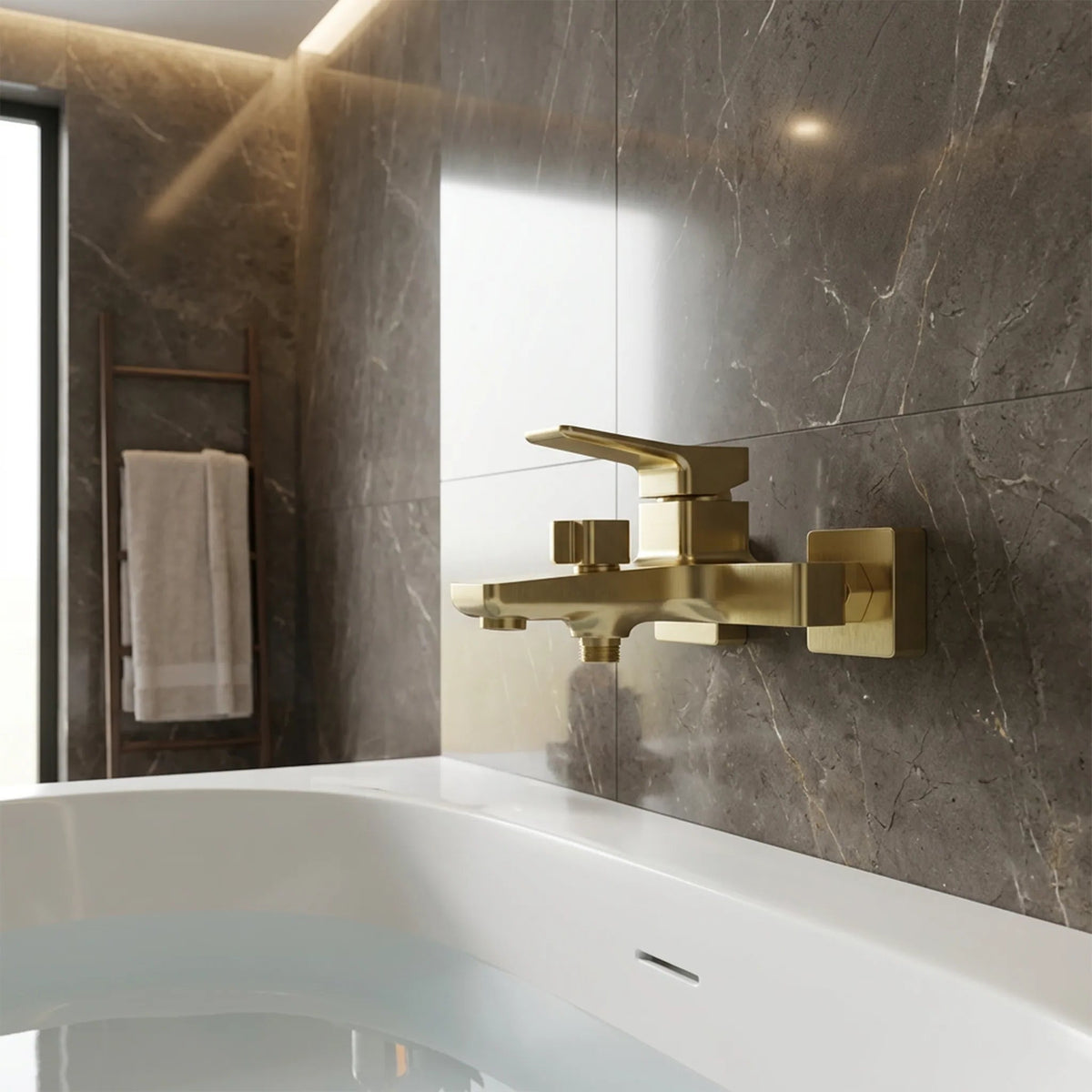A modern brushed gold bathroom faucet with a single lever handle, mounted on a dark gray marble tiled wall above a bathtub.