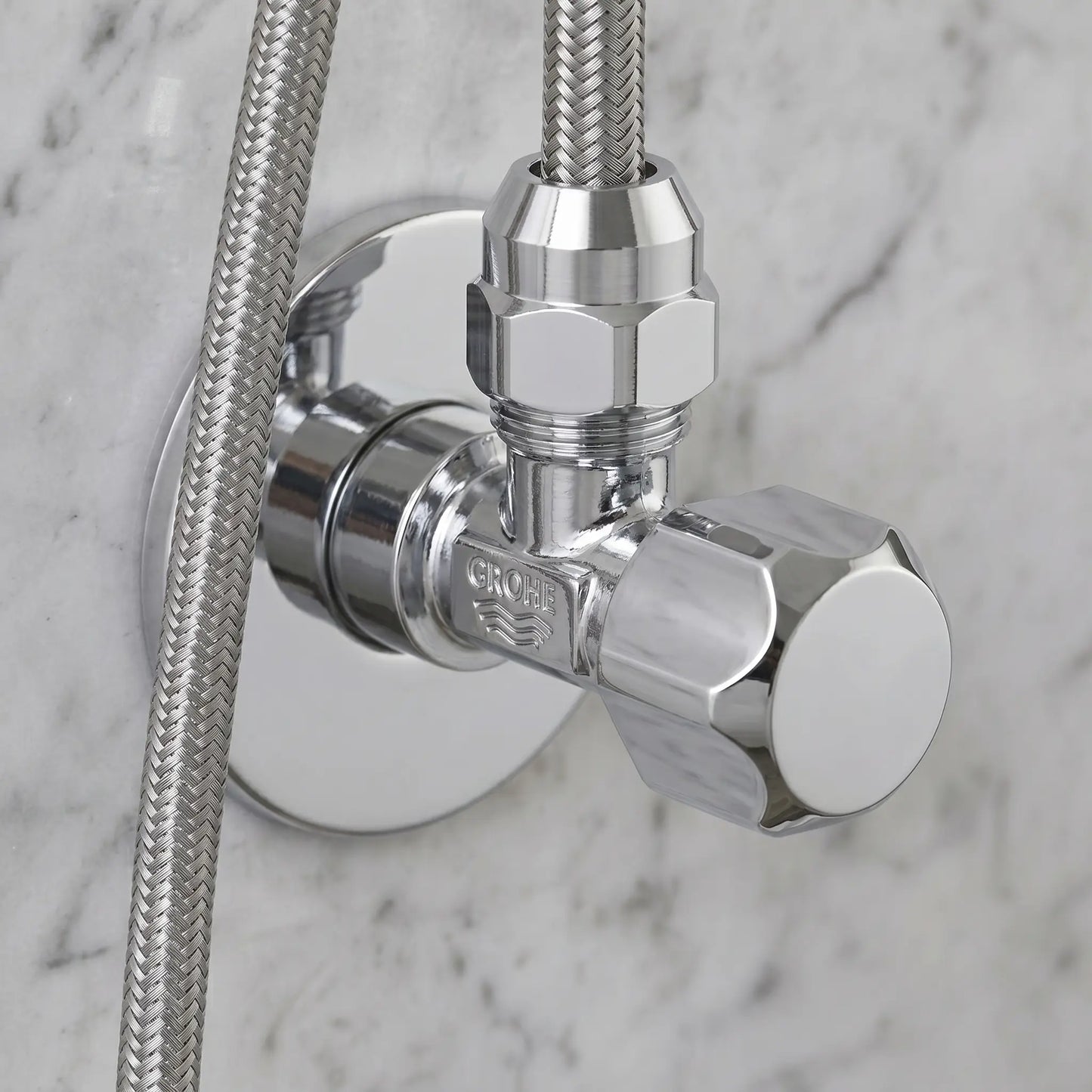 A chrome GROHE angle valve installed on a marble bathroom wall, connected to a stainless steel braided flexible water supply line.