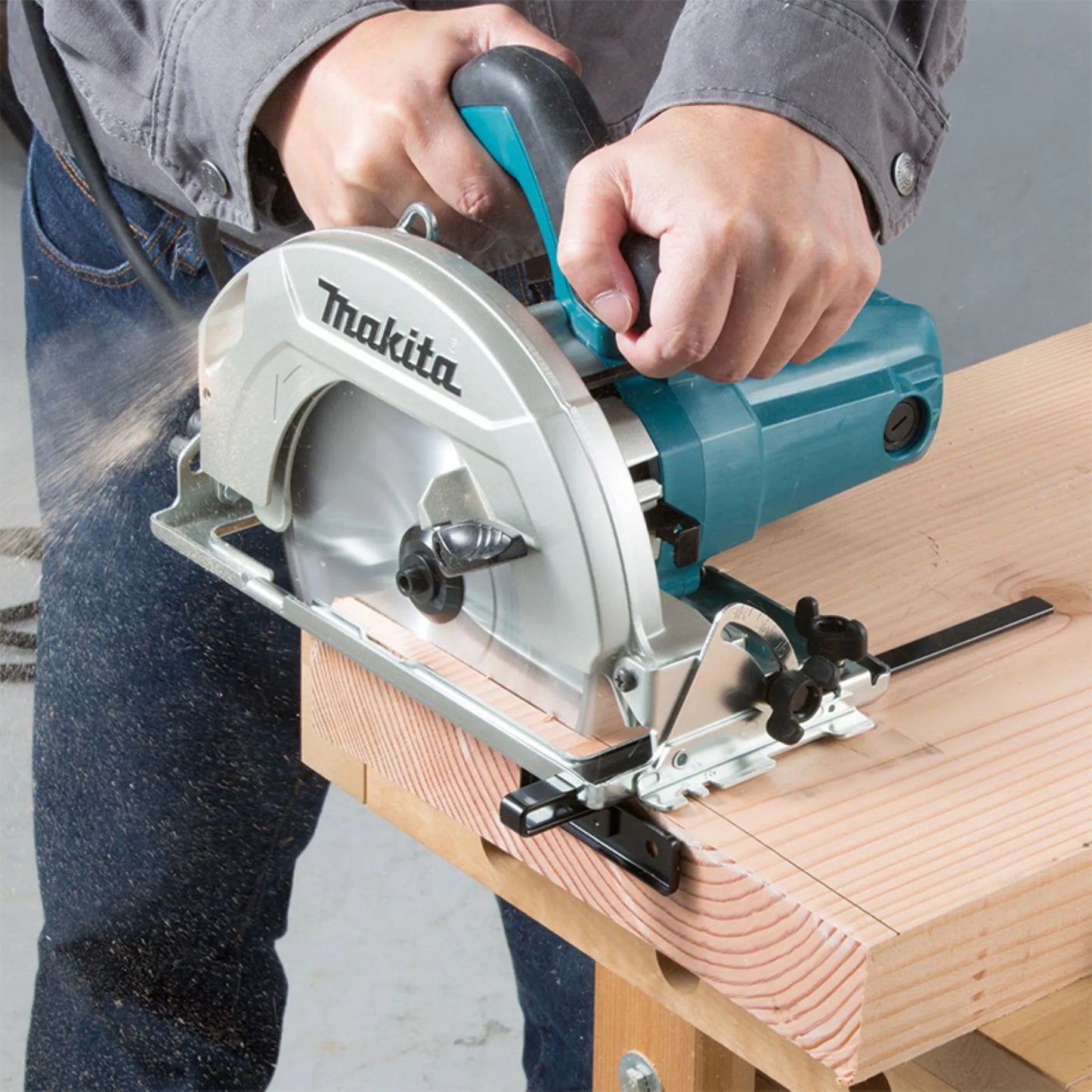 Close-up of a worker using a Makita circular saw with a rip fence guide to make a straight, precise cut through a wooden board.
