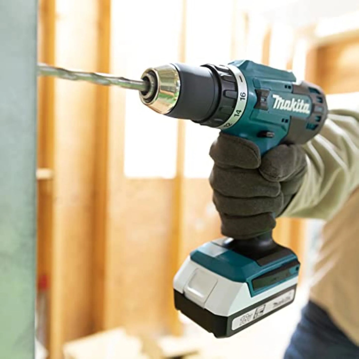 A gloved hand using the Makita 18V cordless driver drill to bore a hole through a metal stud on a construction site.