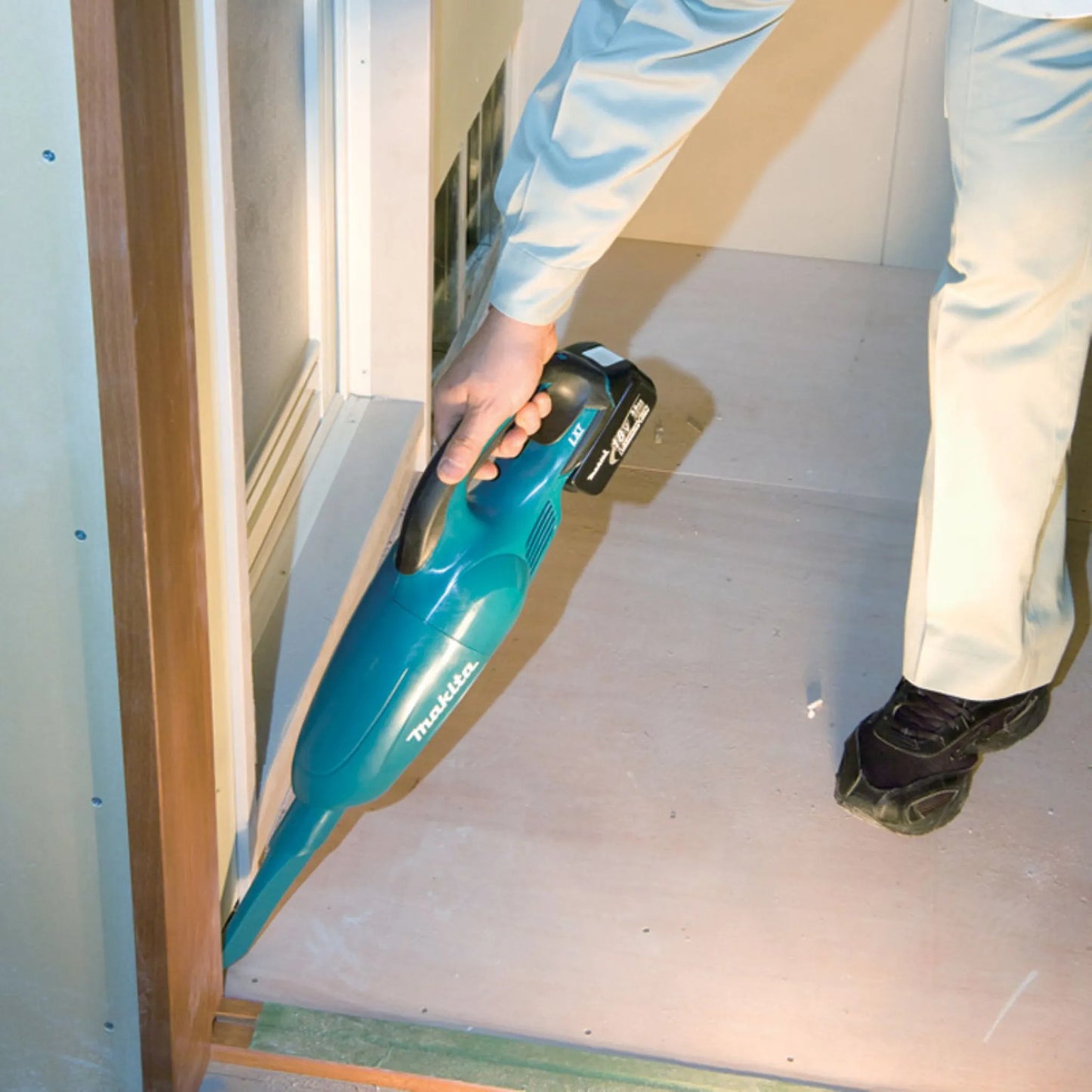User cleaning construction debris from a door track with a blue Makita 18V LXT cordless handheld vacuum.