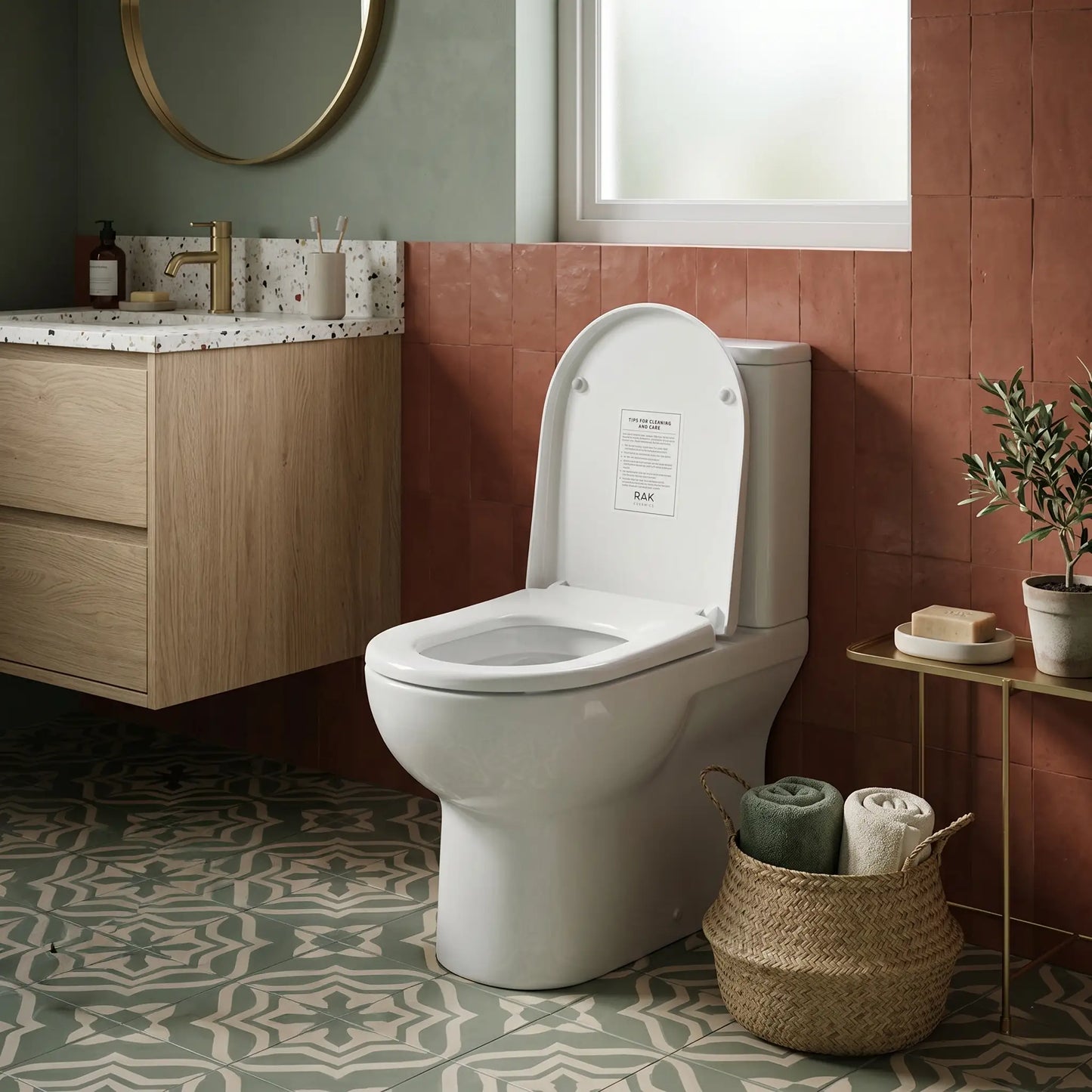 Modern bathroom interior featuring a RAK Ceramics floor-mounted toilet with the Jumeirah soft-close seat cover installed, set against terracotta wall tiles and decorative patterned floor tiles.
