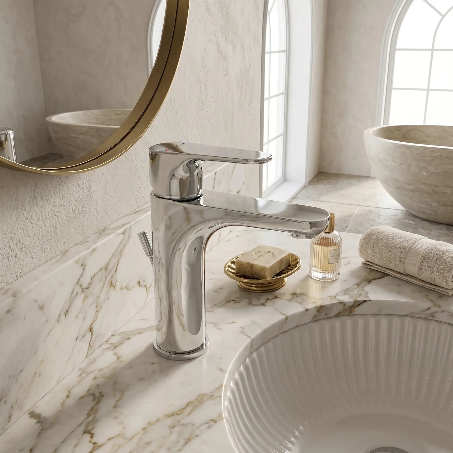 Modern luxury bathroom featuring the VitrA Root Round chrome basin mixer installed on a white-veined marble countertop with a fluted vessel sink, set against a bright, airy background with arched windows.